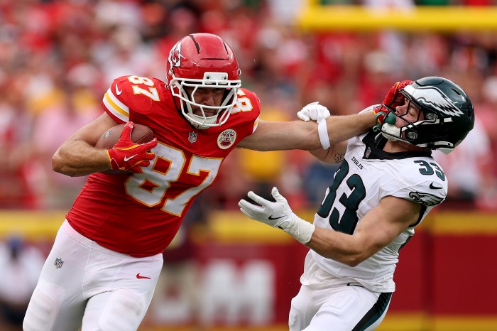 Travis Kelce runs with the ball while stiff-arming a defender with his left arm.