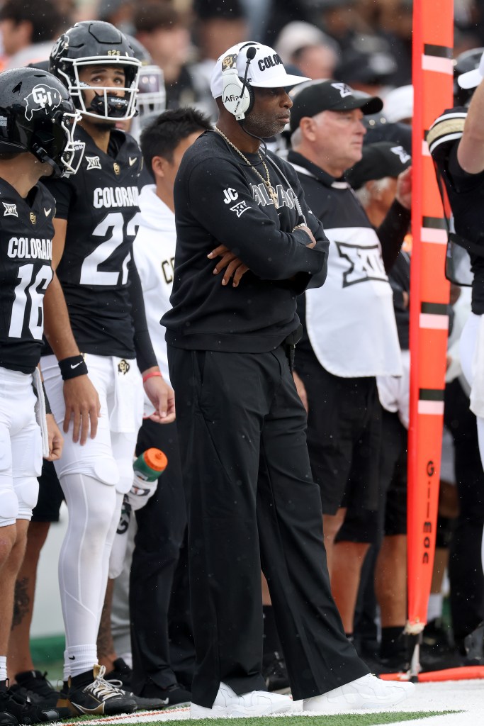 Head coach Deion Sanders of the Colorado Buffaloes, with his arms folded, watches his team from the sidelines.