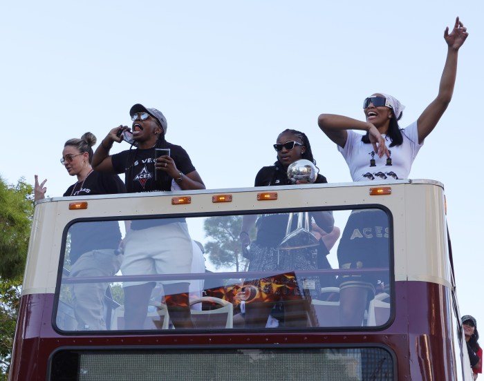 Head coach Becky Hammon (from left), Chelsea Gray, Jackie Young and A'ja Wilson of the Las Vegas Aces ride on top of a bus with the championship trophy during the team's 2022 WNBA championship victory parade and rally in Las Vegas.